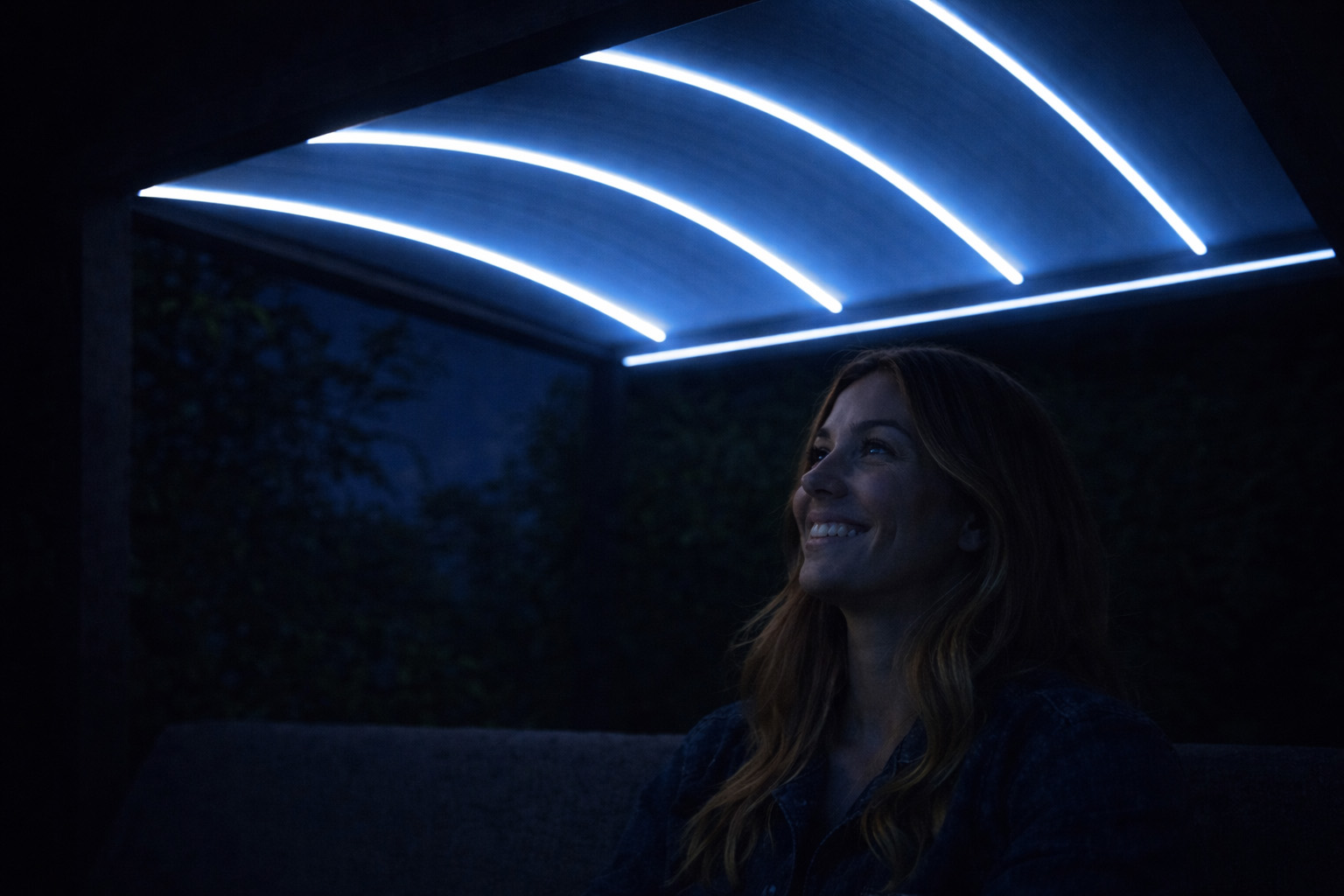Donna sorridente di sera sotto la pergola Tess con illuminazione LED blu